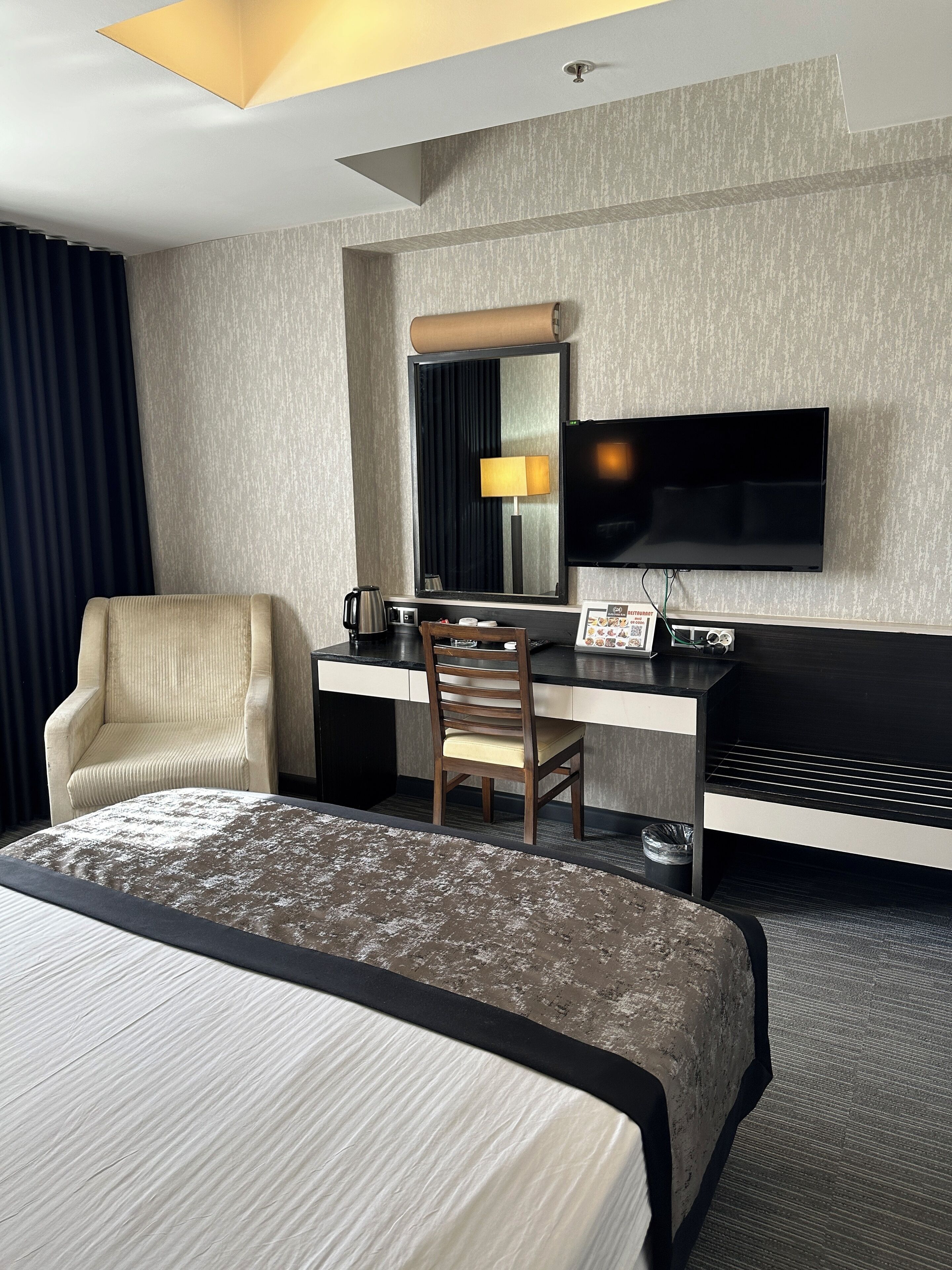 A hotel room with a bed, a desk with a chair, a television, and a mirror.