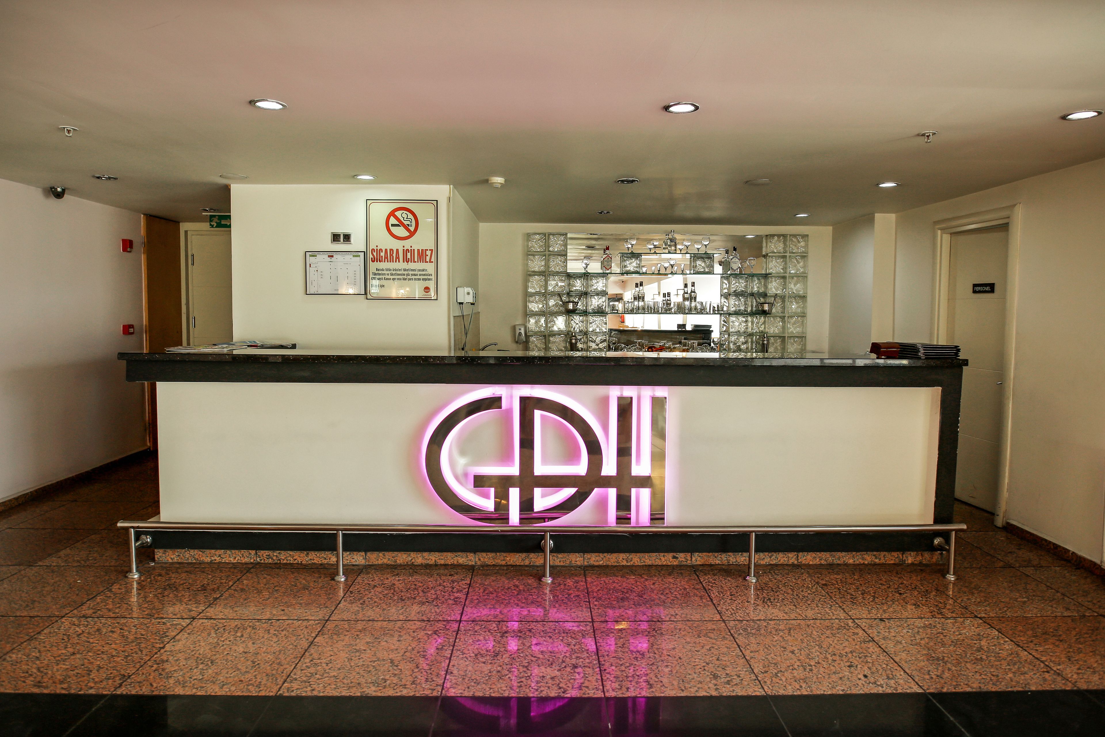 A hotel reception desk with a neon sign, a no smoking sign, and a glass display case with items.