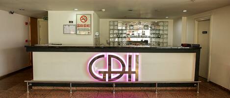A hotel reception desk with a neon sign, a no smoking sign, and a glass display case with items.