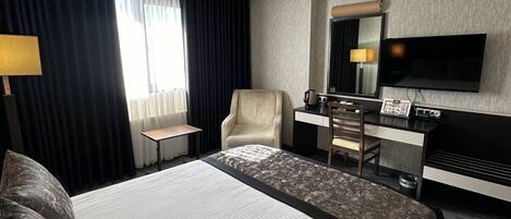 Una habitación de hotel moderna con una cama grande, un escritorio con televisor de pantalla plana, una silla y una cafetera.