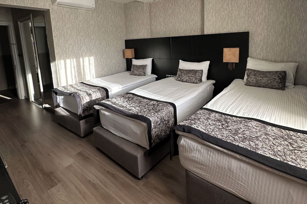 Habitación de hotel con tres camas, ventilador de techo, equipo de aire acondicionado y puerta que da a un balcón.