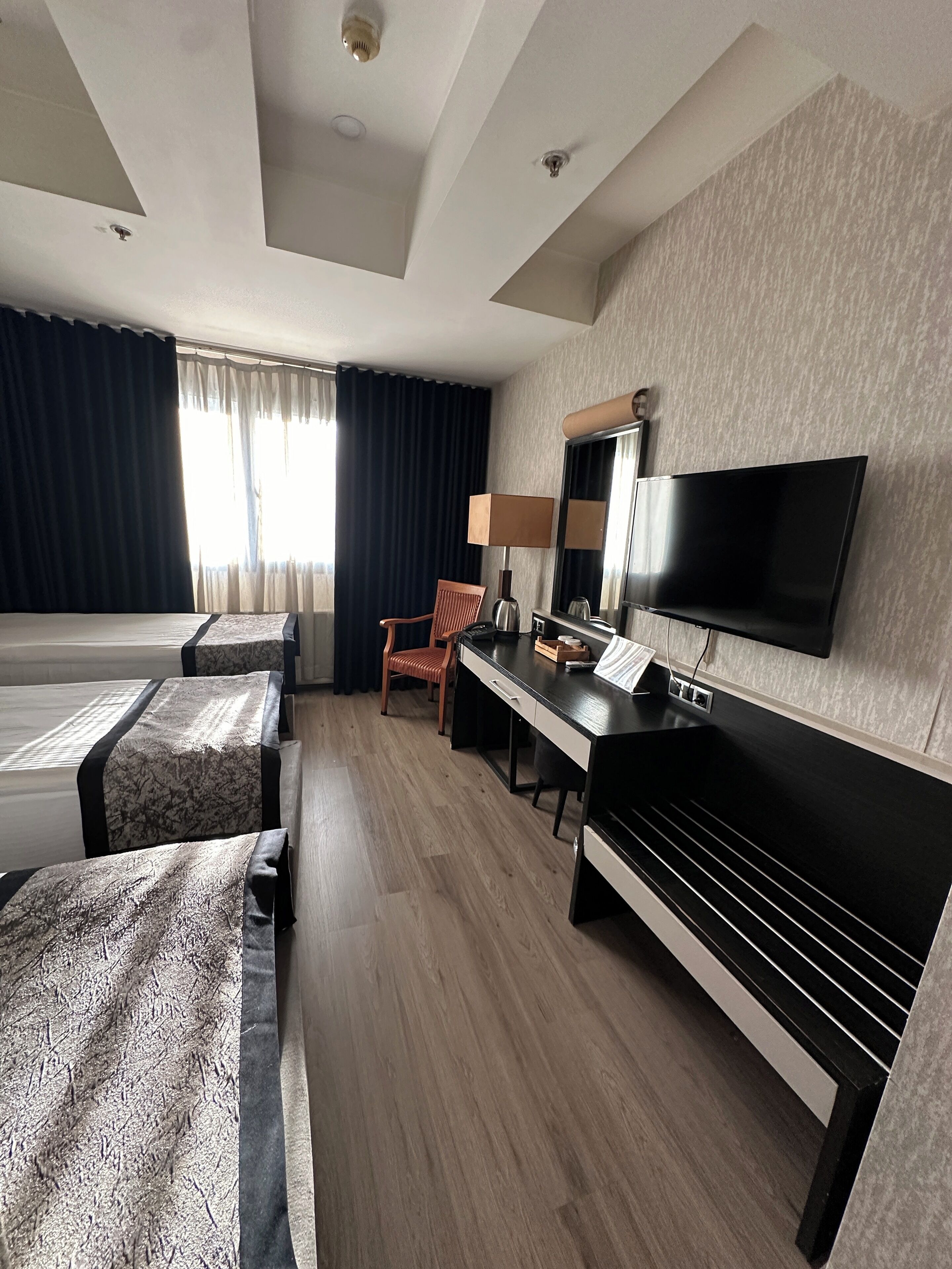 A hotel room with a bed, a desk, a chair, a TV, and a window with curtains.