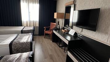 A hotel room with a bed, a desk, a chair, a TV, and a window with curtains.