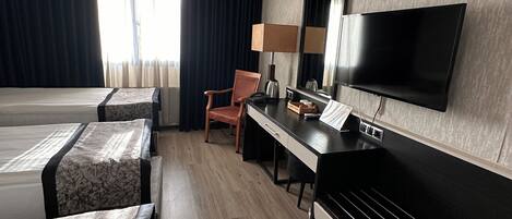 A hotel room with a bed, a desk, a chair, a TV, and a window with curtains.