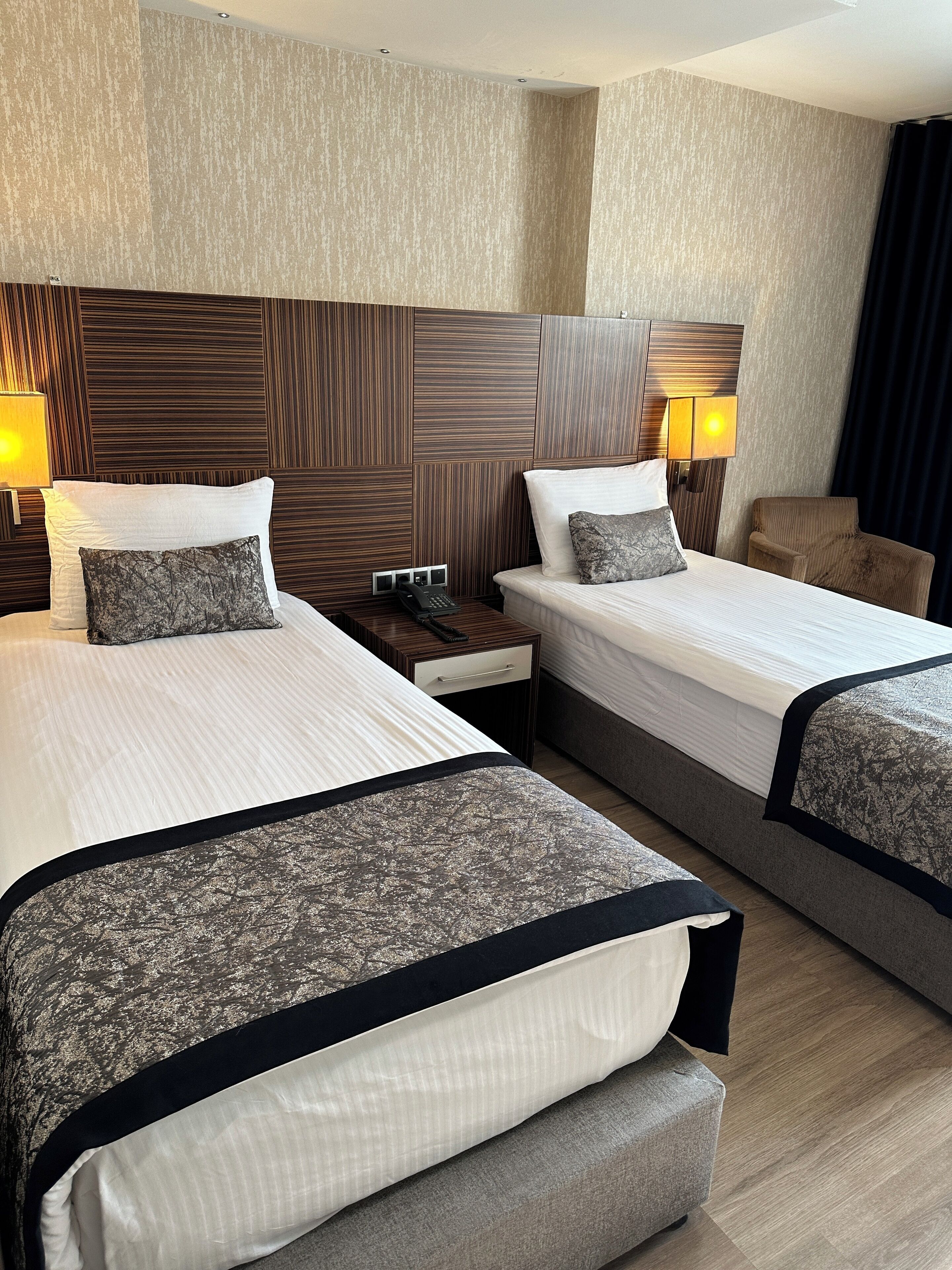 Hotellihuone, jossa on kaksi sänkyä, puinen pääty, yöpöytälamput, yöpöytä ja tuoli.