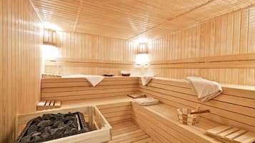 A wooden sauna with benches, a bench with a towel, a small table with a bowl, and a bucket with a brush.