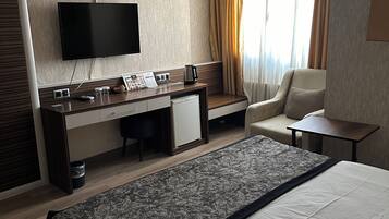 A hotel room with a large bed, a desk with a flat-screen TV, a sofa, and a small table.
