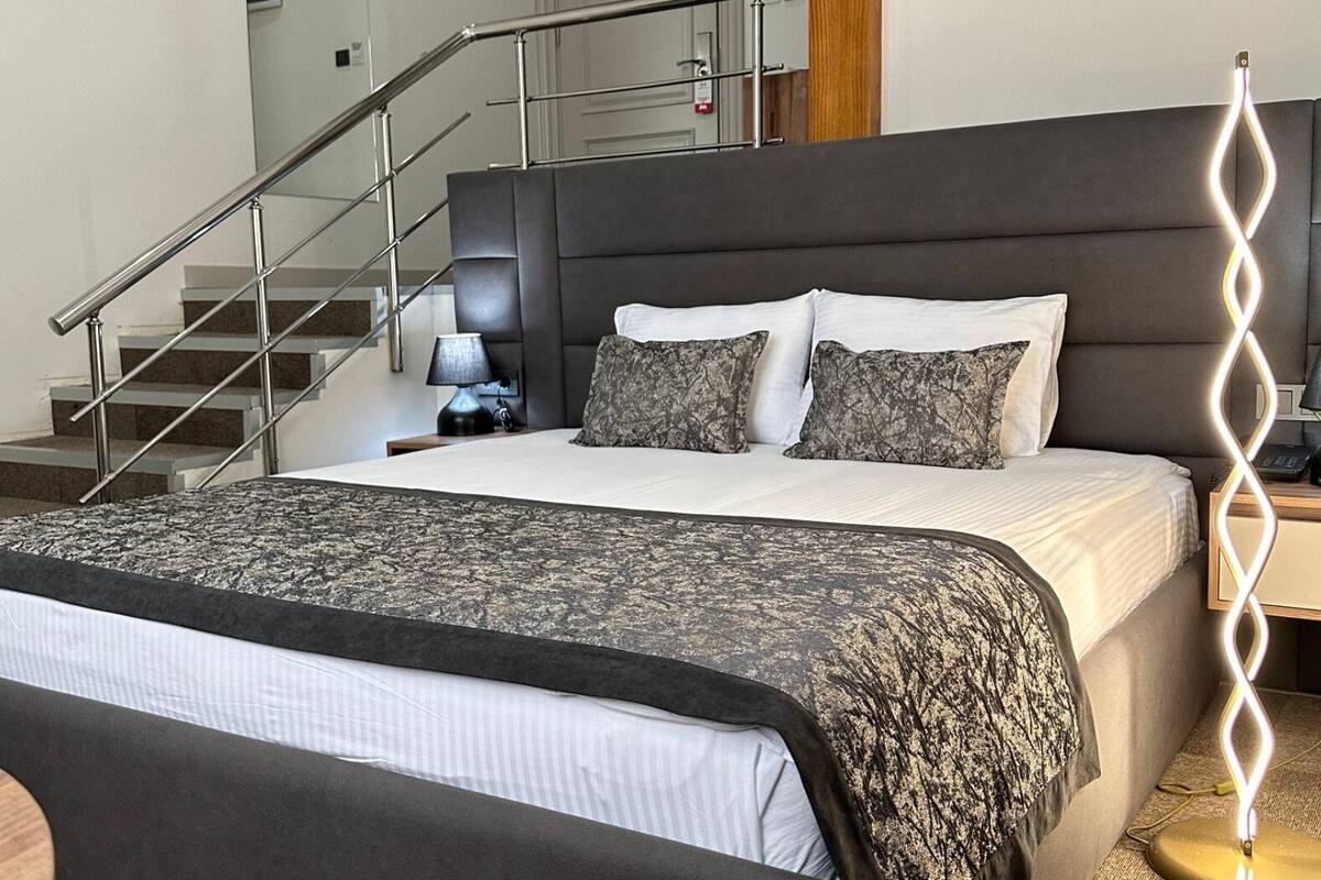 Un dormitorio moderno con una cama grande, una mesita de noche, una lámpara, una escalera y un pilar de madera.