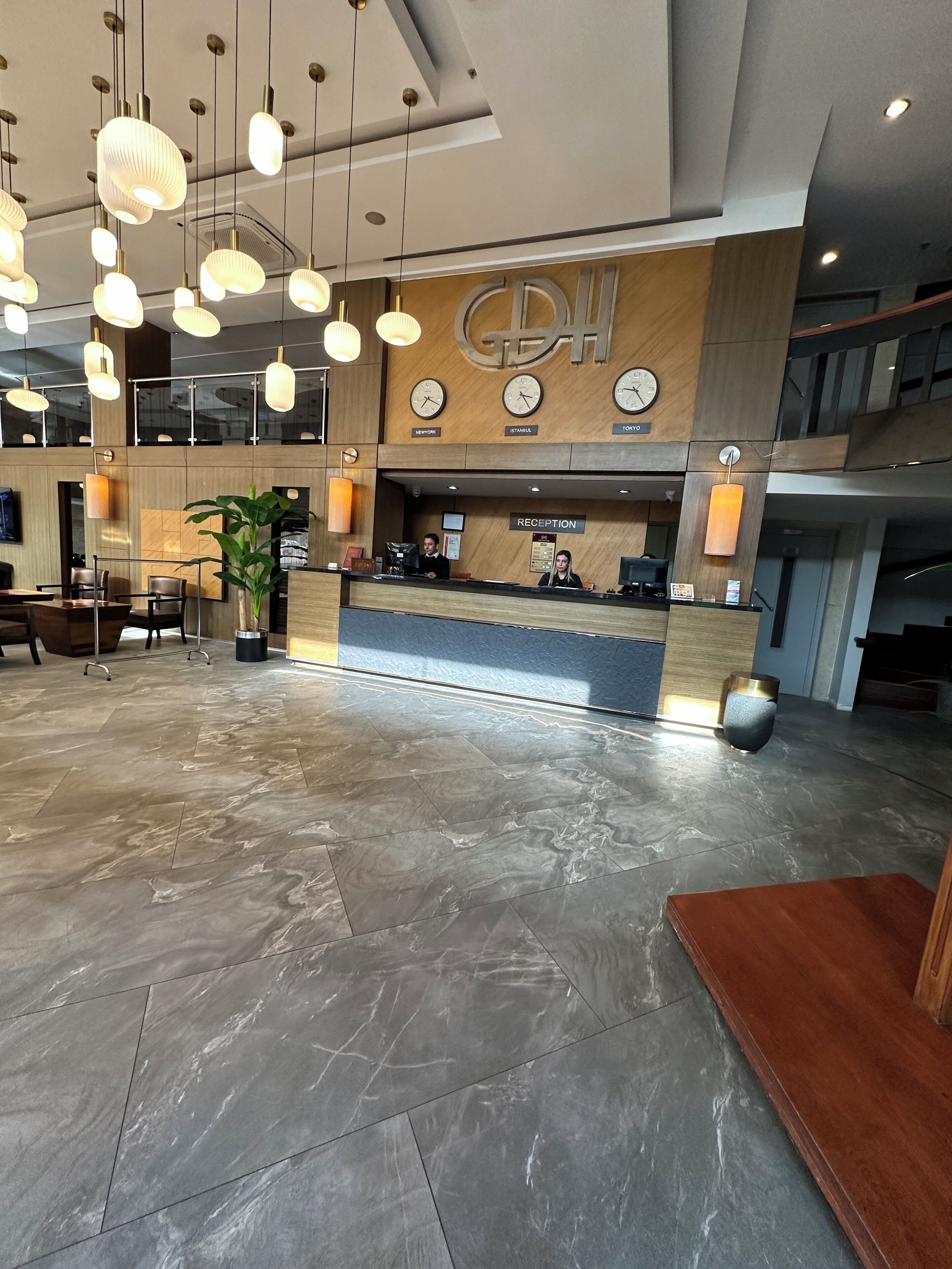 A spacious lobby with a reception desk, modern pendant lighting, and a large potted plant.