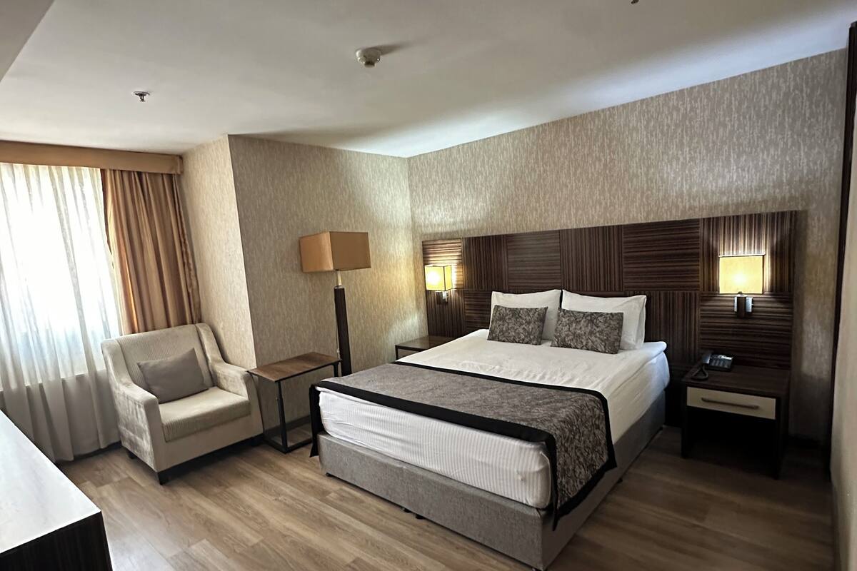 Una habitación de hotel moderna con una cama grande, una silla, un escritorio y dos mesitas de noche con lámparas.