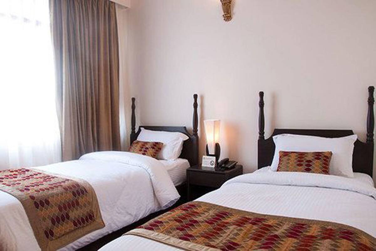 A hotel room with two beds, a nightstand with a lamp, and a window with curtains.