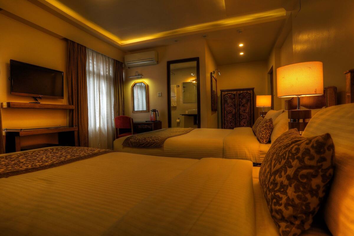 A hotel room with two beds, a TV, a desk, and a bathroom visible through a door.
