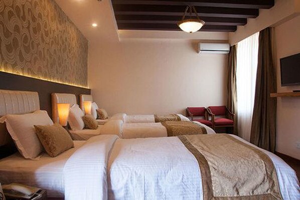 A hotel room with two beds, a TV, a red chair, and a patterned wall.
