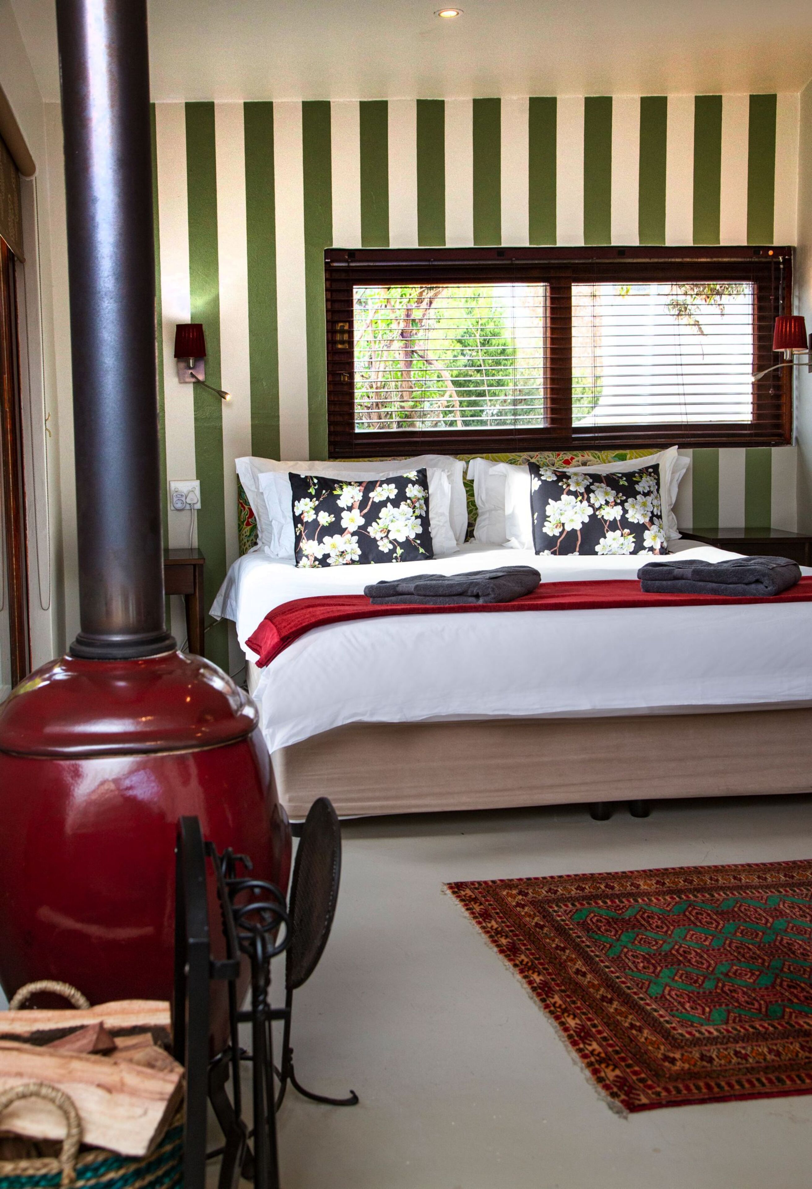 A bedroom with a bed, a red heater, a window with blinds, and a patterned rug.