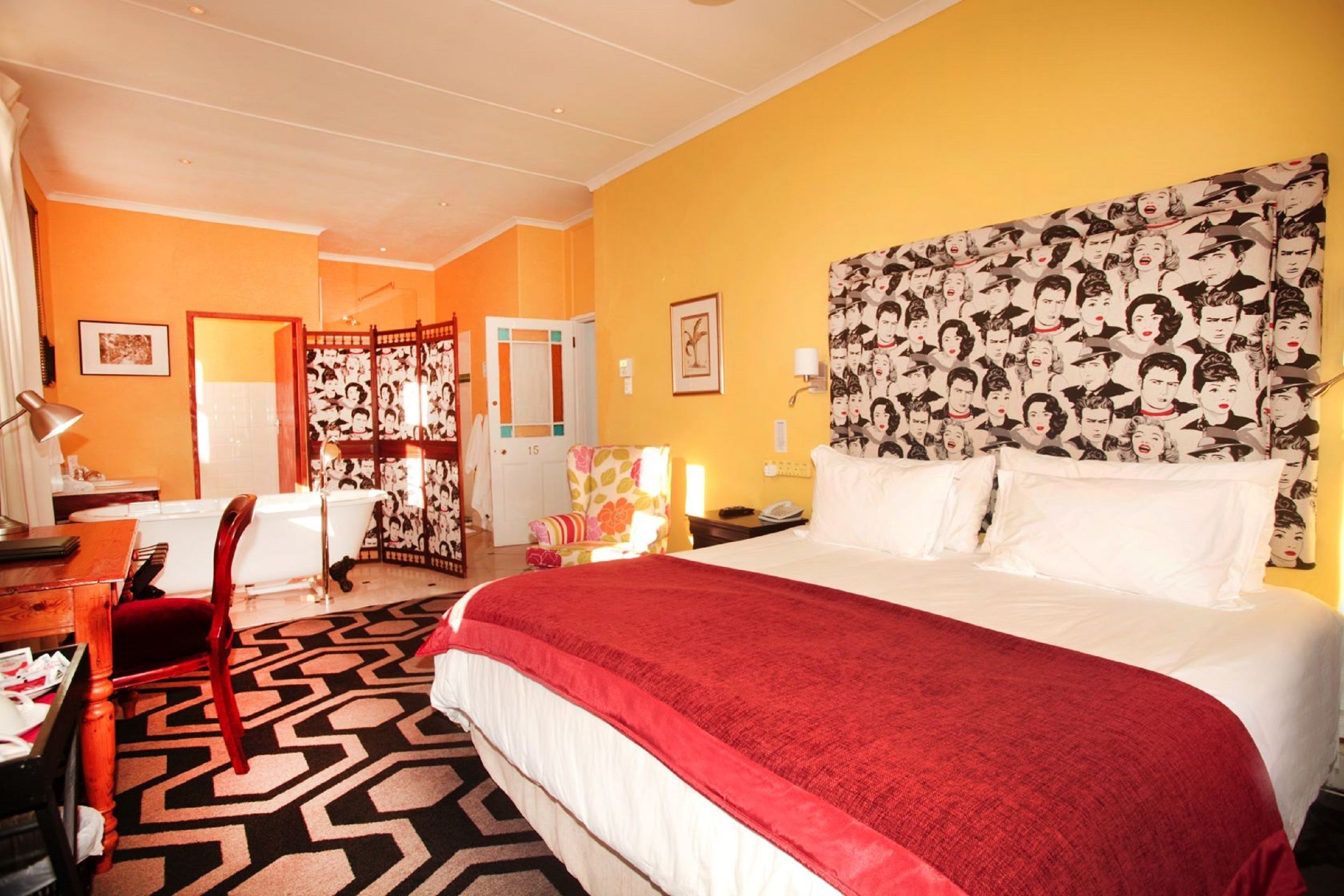 A hotel room with a large bed, a desk with a chair, a bathroom, and a partition with a floral pattern.