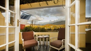 A balcony with two chairs and a small table, overlooking a scenic landscape with mountains and a village.
