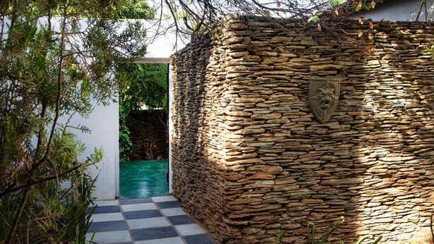 A stone wall with a lion crest, a checkered pathway, and a green pool area.