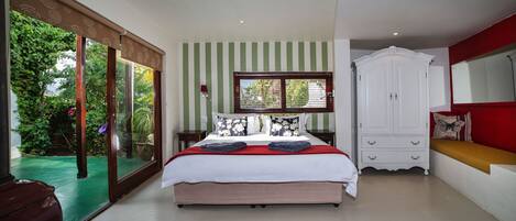 A bedroom with a bed, a white wardrobe, a window with blinds, and a view of greenery outside.