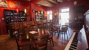 A bar area with wooden tables and chairs, a piano, and a bar stocked with bottles.