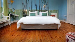 A bedroom with a large bed, a bedside table, a chair, a mirror, and a wall with tree-like decorations.