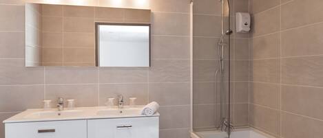 A modern bathroom with a large mirror, two sinks, a shower, and a towel rack.
