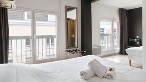 A hotel room with a large bed, a small table, a chair, and a window with a view of buildings. - Lille City Hotel (Lille)
