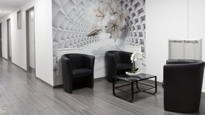 A modern office space with a geometric wall design, two black leather chairs, a glass coffee table, and a white vase with flowers. - Lille City Hotel (Lille)