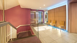 A modern hotel lobby with a staircase, elevators, and seating area. - Lille City Hotel (Lille)