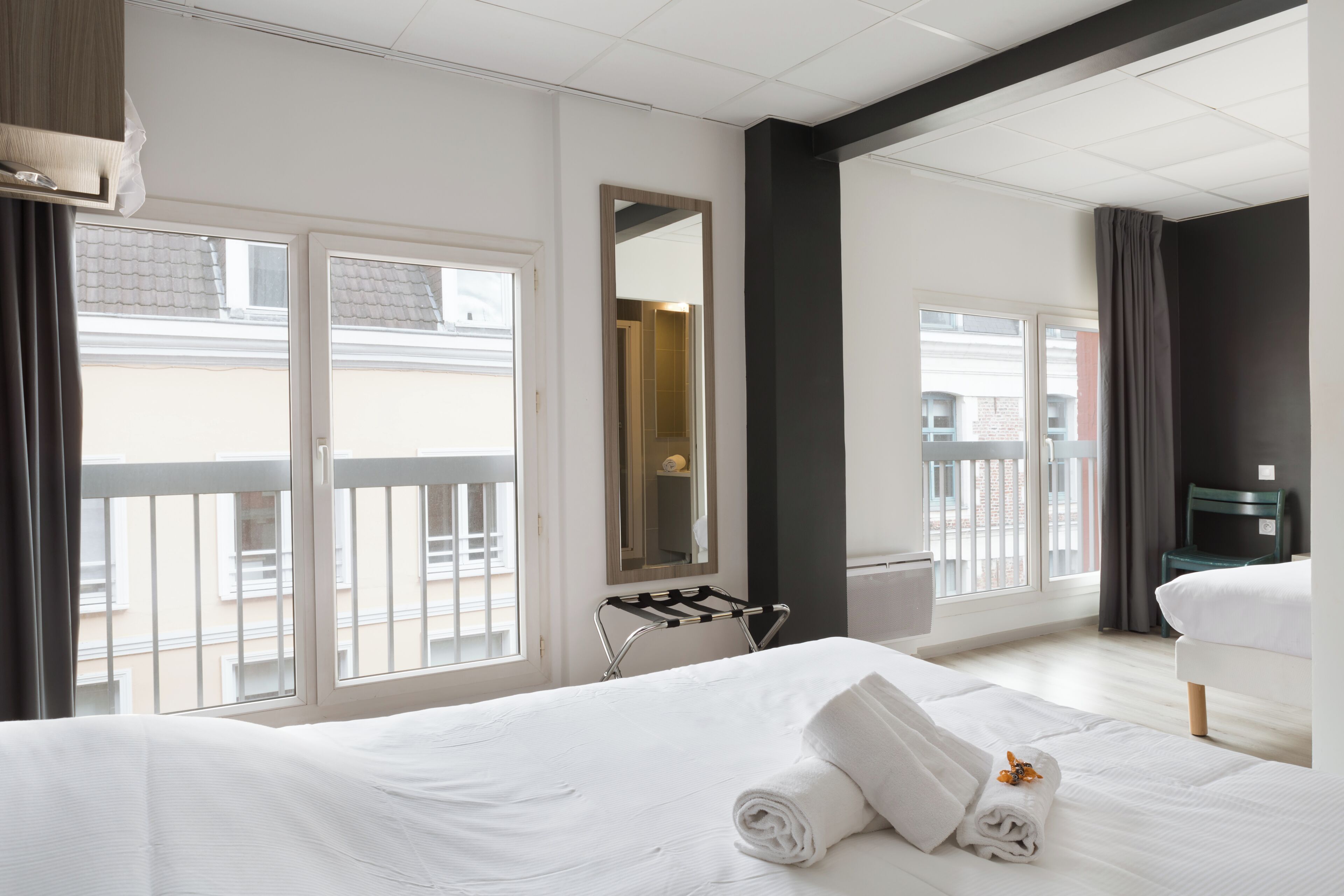 A hotel room with a large bed, a small table, a chair, and a window with a view of buildings.