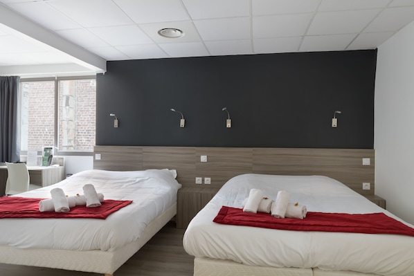 Habitación de hotel con dos camas, un escritorio y ventana con vista a un edificio de ladrillo.