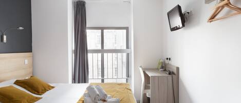 Habitación de hotel con cama, escritorio, televisión y ventana con cortinas.