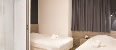 A hotel room with two beds, a shower, a bedside table, and a window with curtains.