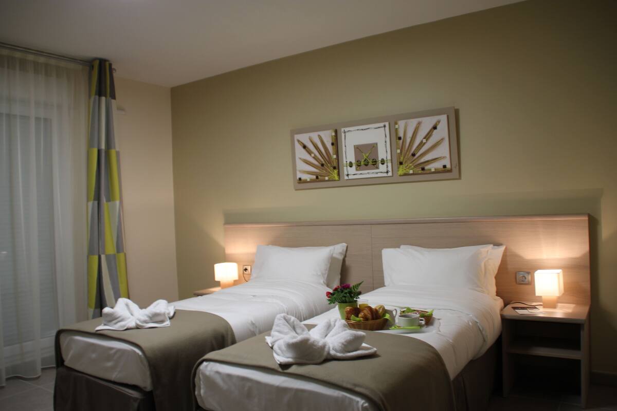 A hotel room with two beds, a nightstand with a lamp, and a wall art piece above the beds.