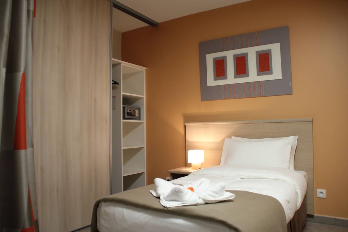 A hotel room with a bed, a nightstand, a lamp, a wardrobe, and a wall art piece.