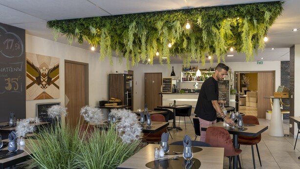 A modern restaurant with hanging plants, neatly arranged tables, and a bar area. - The Originals Boutique, Hôtel l'Occitan, Aubagne Nord (La Destrousse)