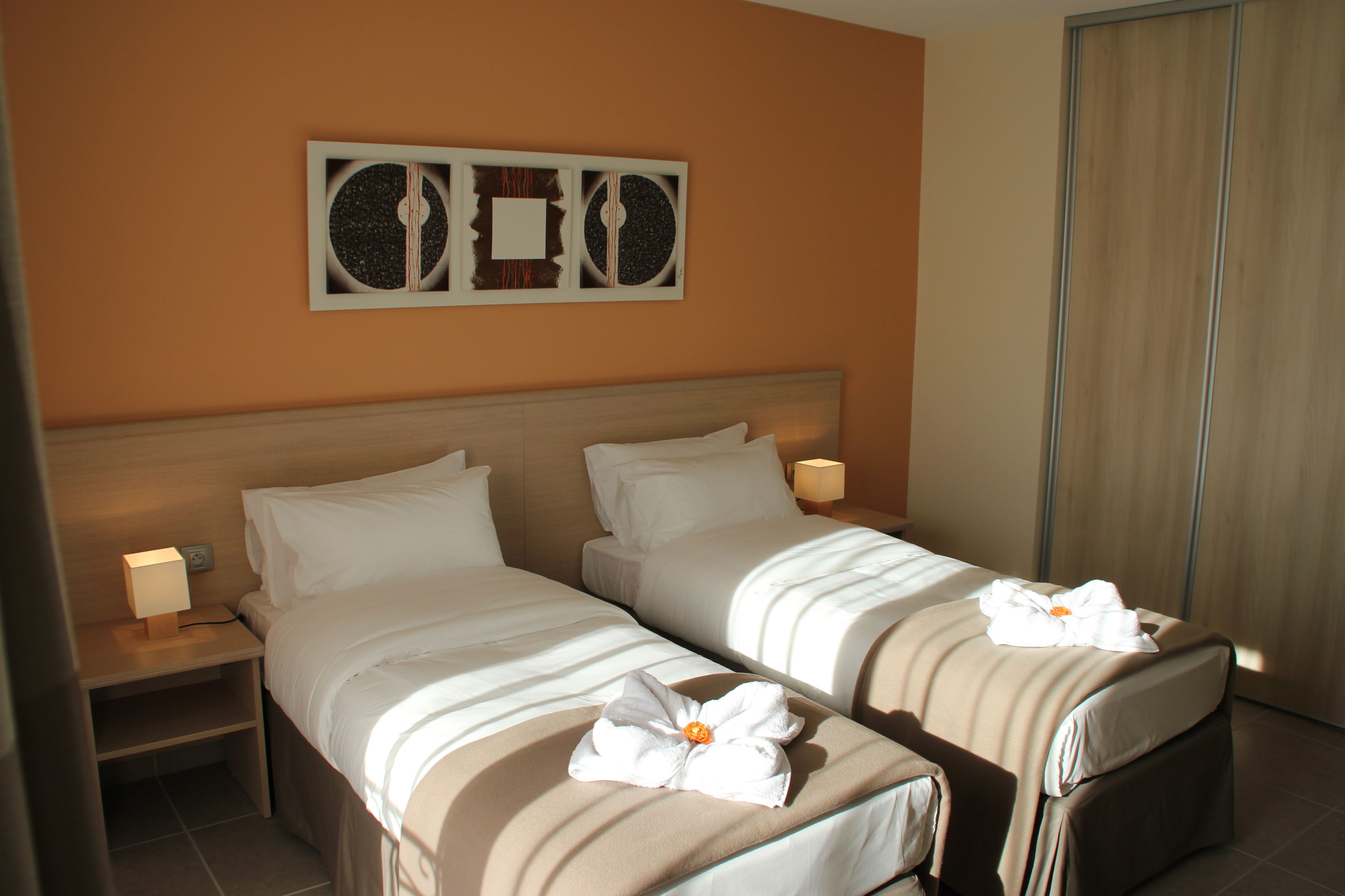 A hotel room with two beds, a nightstand with a lamp, and a wall art piece.