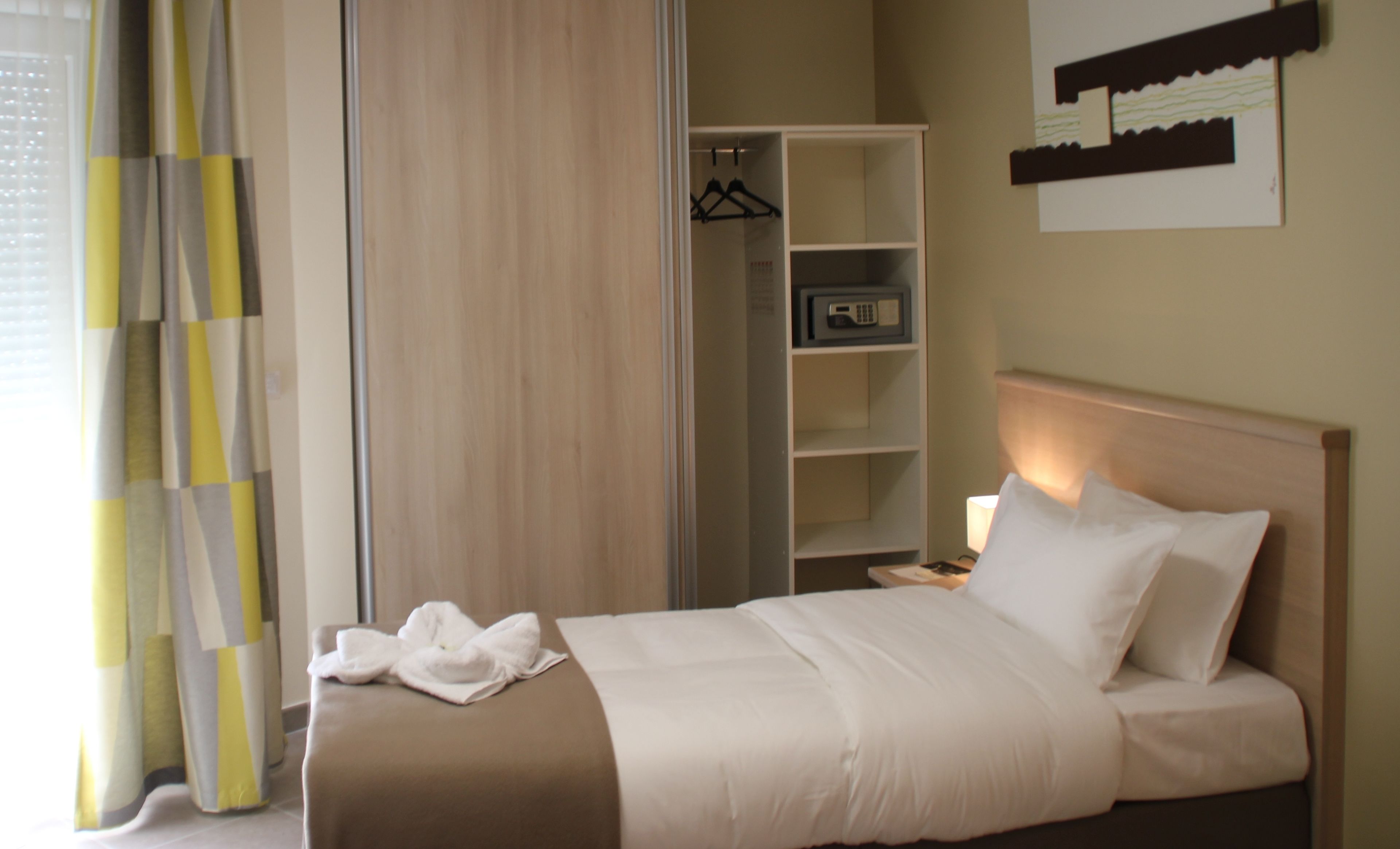 Habitación de hotel con cama, mesita de noche, lámpara, armario y estante con una radio.