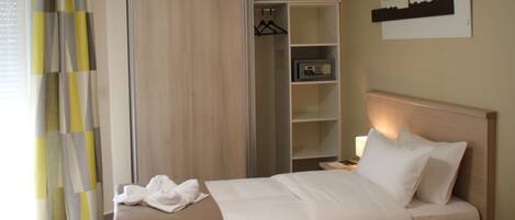 Habitación de hotel con cama, mesita de noche, lámpara, armario y estante con una radio.
