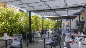 An outdoor patio area with tables and chairs, some covered by umbrellas, and a menu board visible in the background. - The Originals Boutique, Hôtel l'Occitan, Aubagne Nord (La Destrousse)