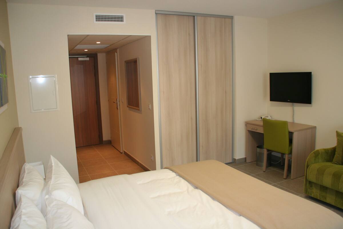 A hotel room with a bed, a desk, a chair, a television, and a sliding door.