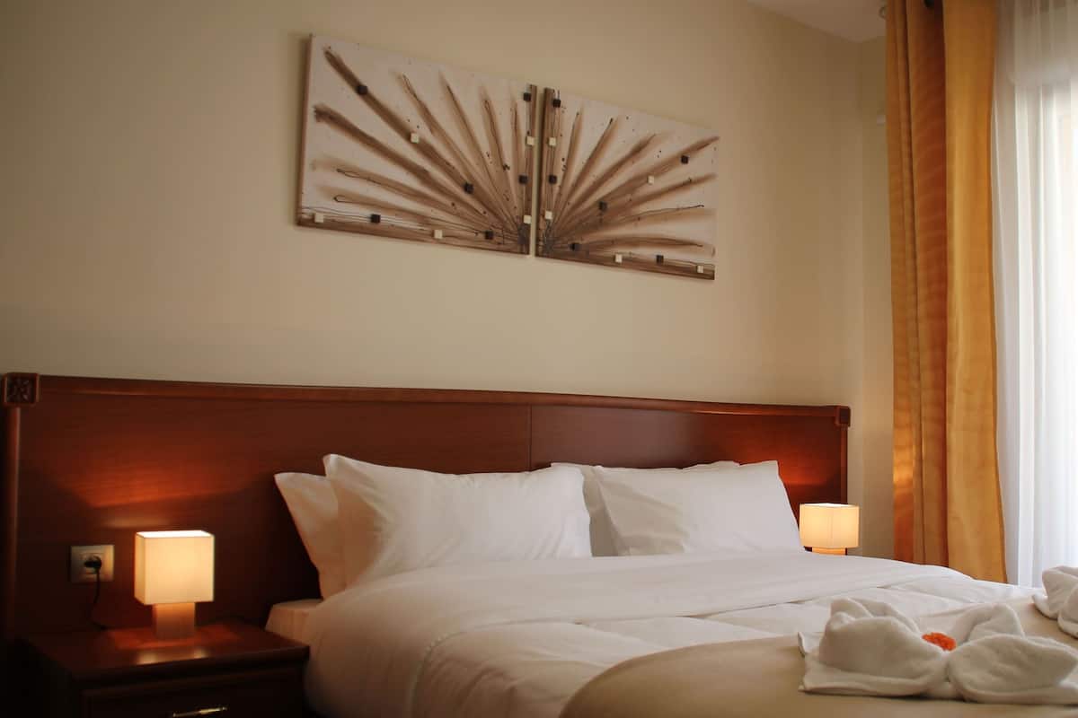 Una habitación de hotel con una cama grande, dos lámparas de noche, una obra de arte en la pared y una ventana con cortinas.