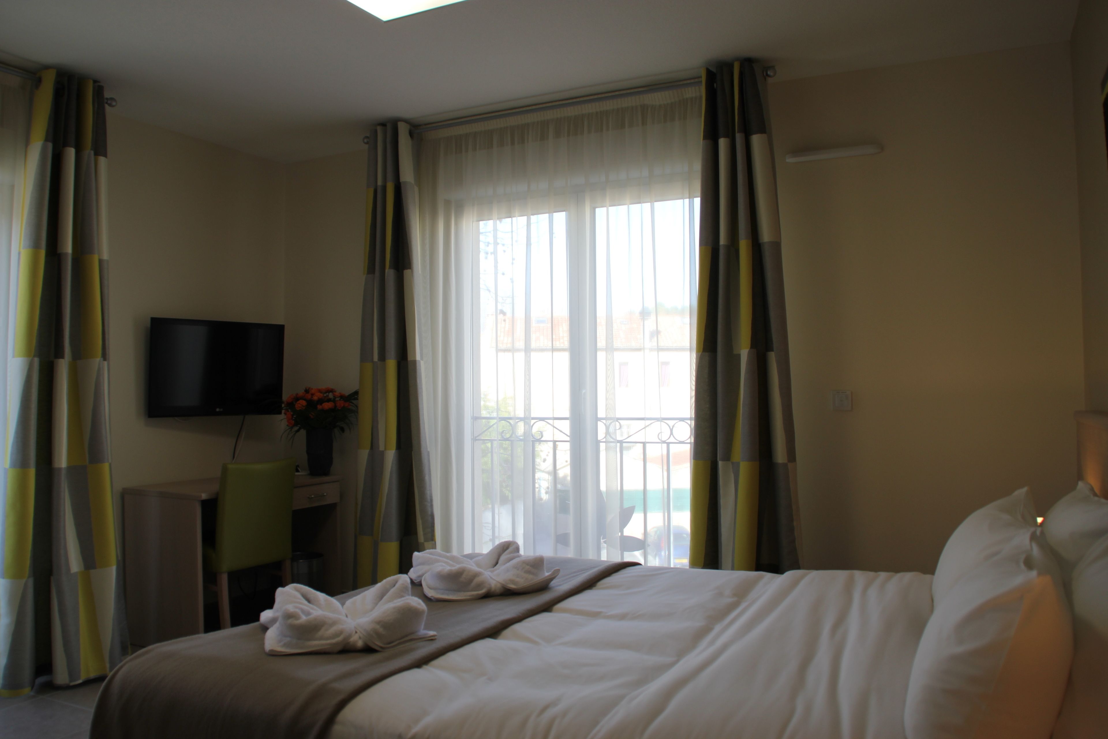 A hotel room with a bed, a desk with a TV, and a window with curtains.