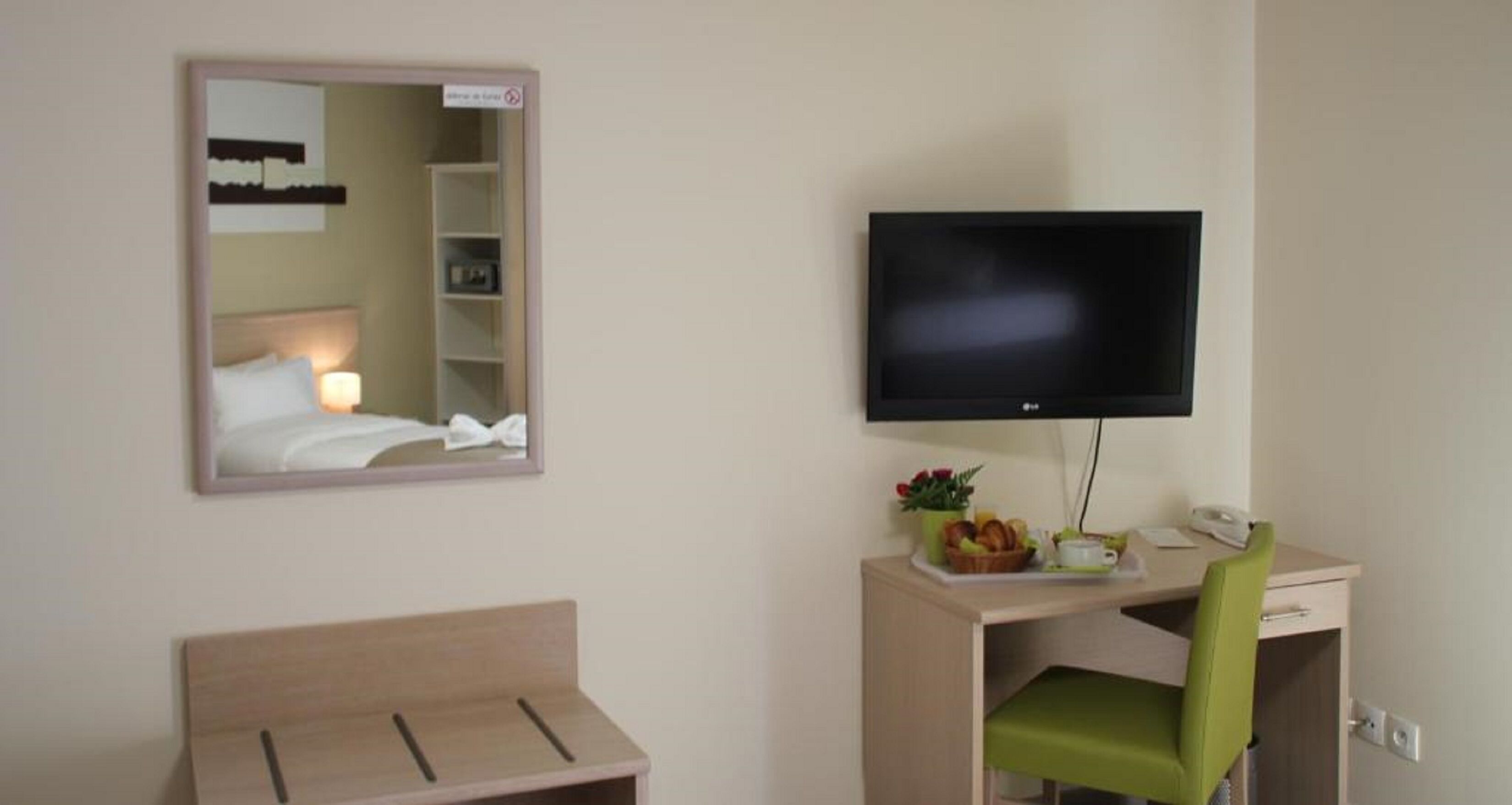 Una habitación de hotel con cama, un escritorio con silla, televisor y espejo.