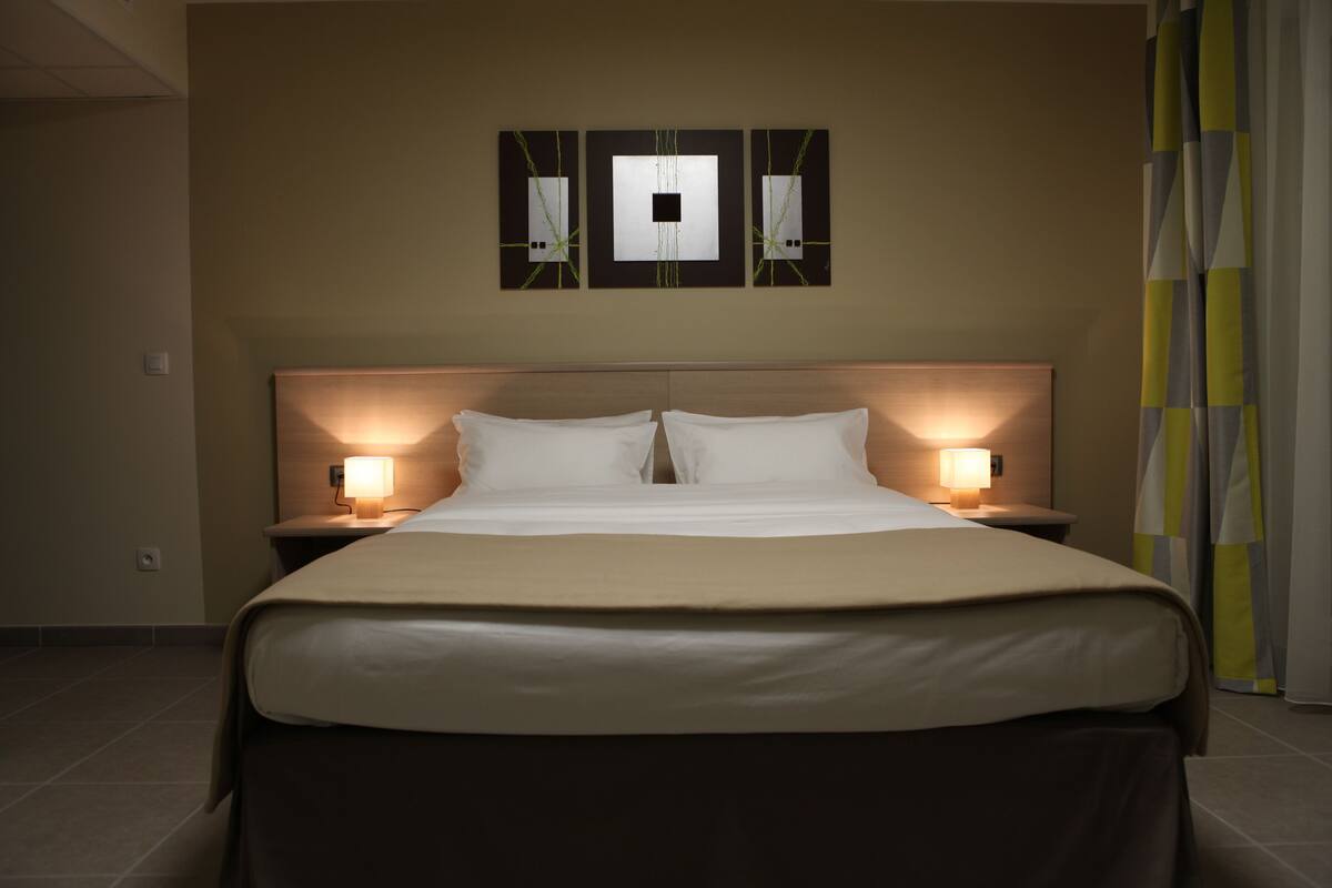 A hotel room with a large bed, two bedside lamps, and a wall-mounted artwork above the bed.