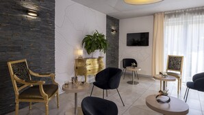 A modern hotel room with a large plant, a gold dresser, and a TV mounted on the wall. - The Originals Boutique, Hôtel l'Occitan, Aubagne Nord (La Destrousse)