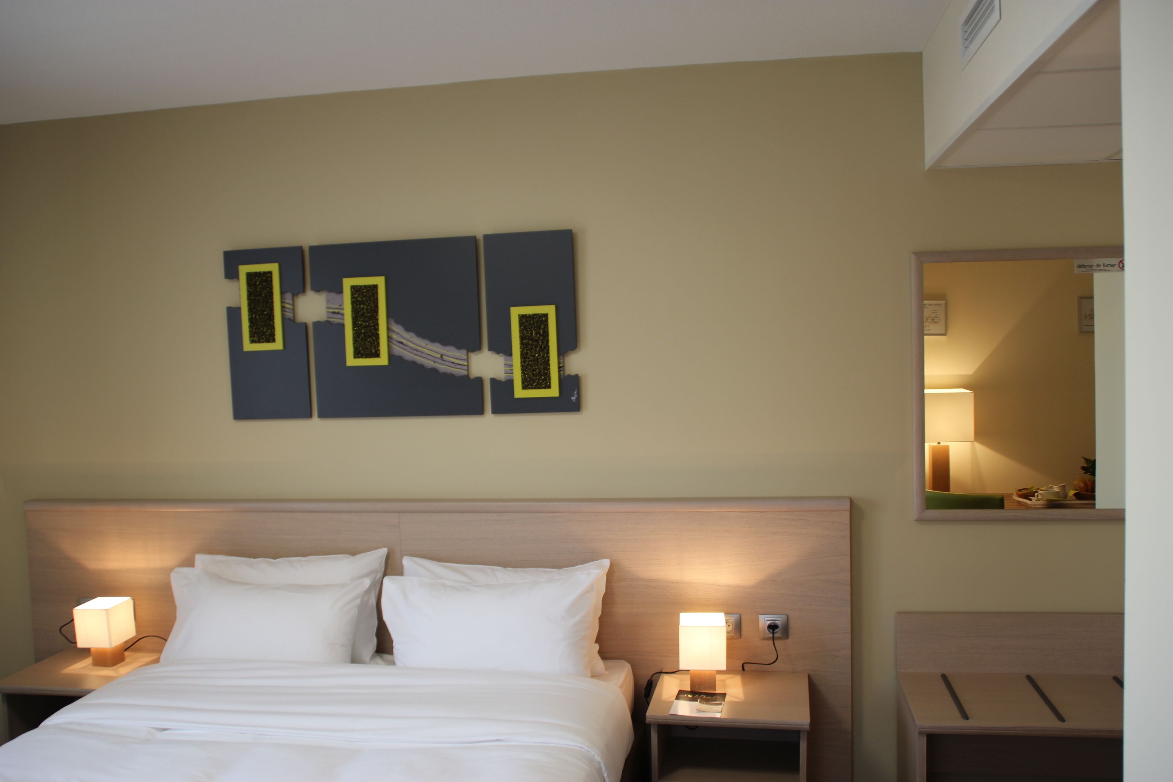 A hotel room with a bed, two bedside tables with lamps, a wall-mounted artwork, and a mirror.