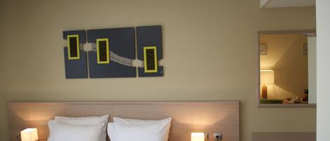 Een hotelkamer met een bed, twee nachtkastjes met lampen, een kunstwerk aan de muur en een spiegel.