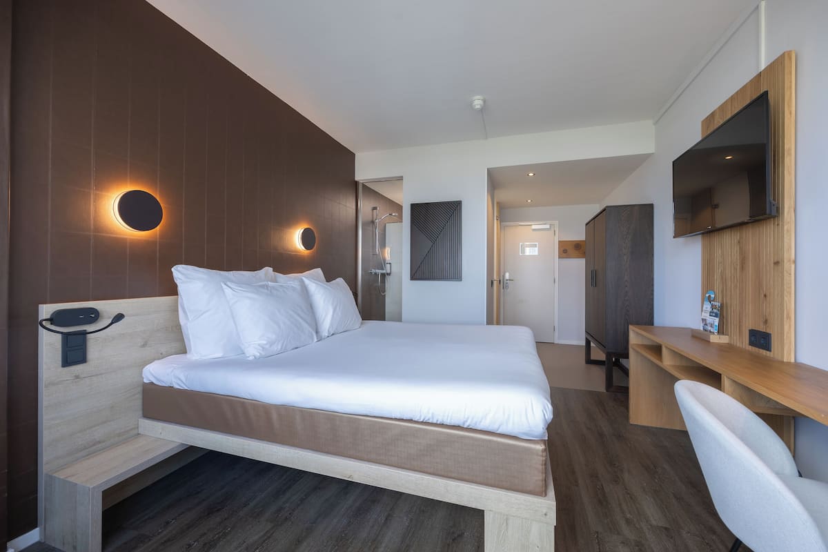 Ein modernes Hotelzimmer mit einem großen Bett, einem Schreibtisch und einem an der Wand befestigten Fernseher.