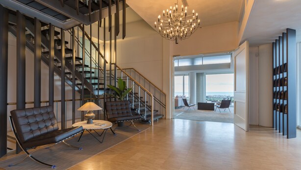 Amplia sala de estar con una escalera moderna, un candelabro y vistas al exterior.