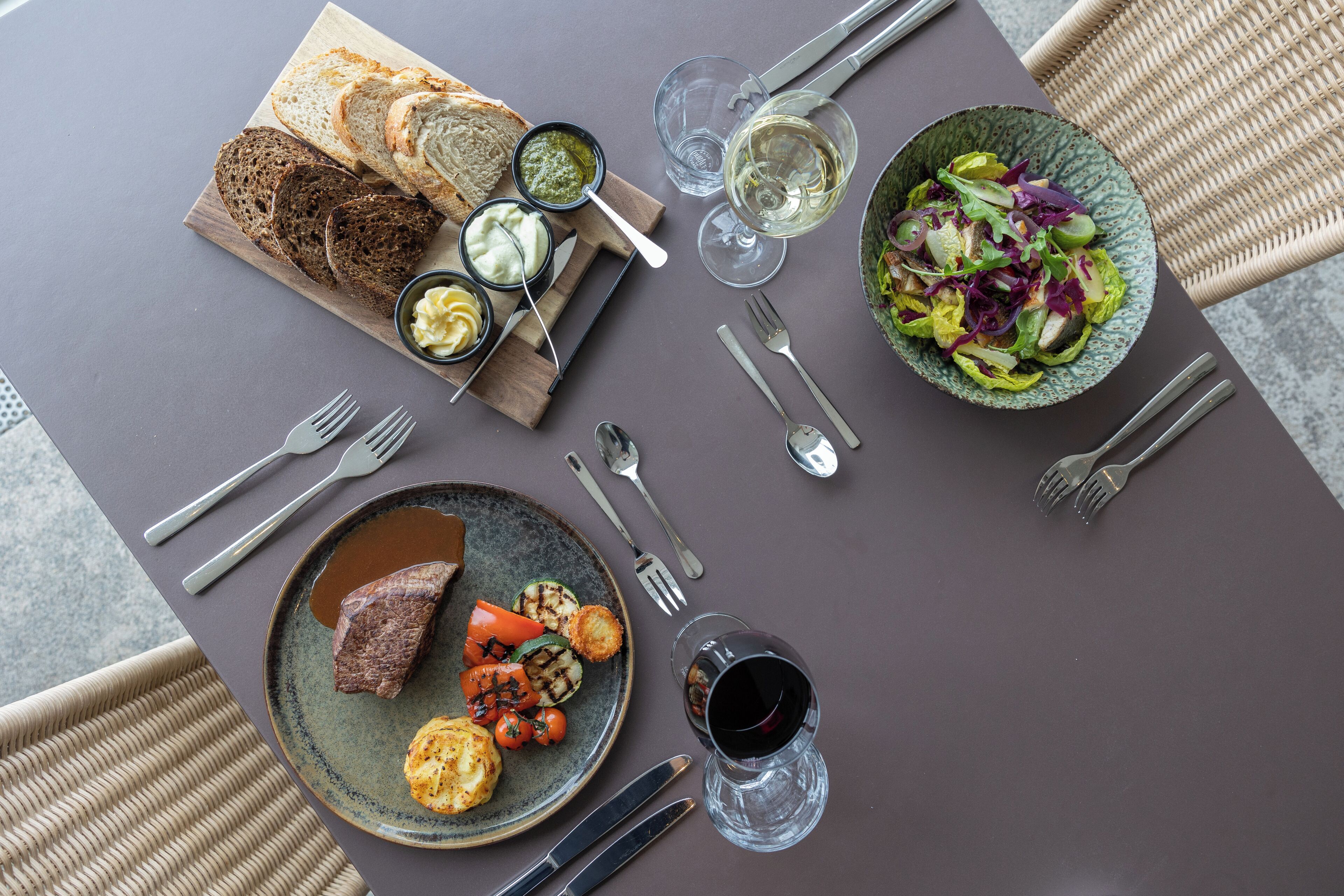 A table set with various dishes, including bread, salad, and meat, along with wine glasses and cutlery.